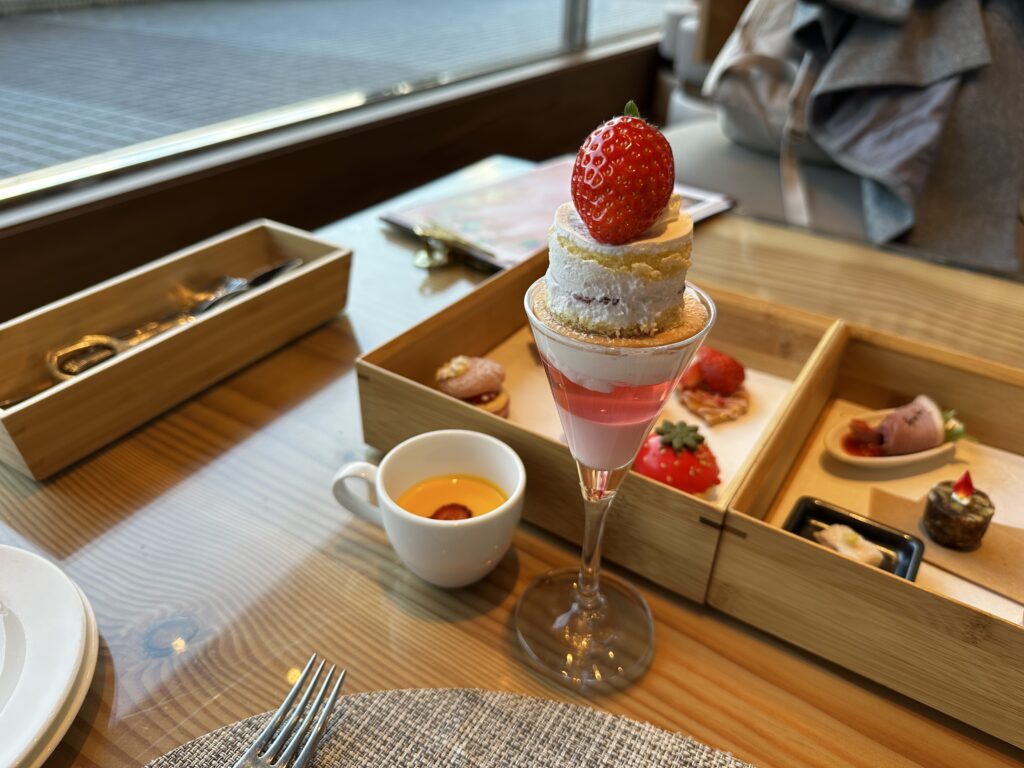 ヒルトン東京ベイのアフタヌーンティー。グラスに盛られたデザートと、木箱に入った軽食が並ぶ窓際の席